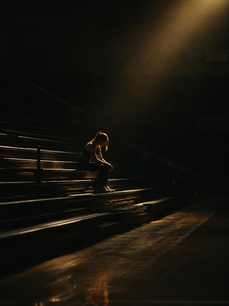 Illustrative image: a woman sitting alone on bleachers in a shaft of light